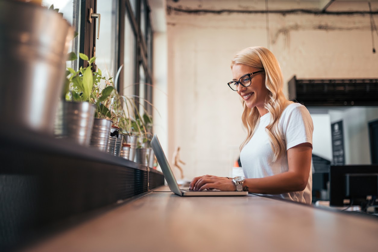 Woman working on laptop in coffee shop for her side hustle to make extra money